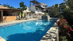 A swimming pool with a clear blue water, surrounded by a stone deck and some greenery. - Pousada Pérola do Mar (Tamandaré)
