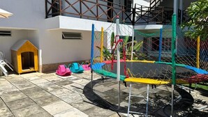 A playground with a trampoline, a small wooden playhouse, and a fenced area. - Pousada Pérola do Mar (Tamandaré)