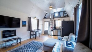 A cozy loft-style living room with a flat-screen TV, a dining area, and a kitchen.