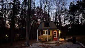 A small, single-story cabin with a red door and windows, surrounded by trees.