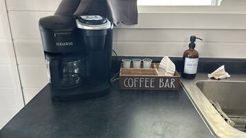 A kitchen counter with a Keurig coffee maker, a coffee bar sign, a dish soap bottle, and a paper towel dispenser.
