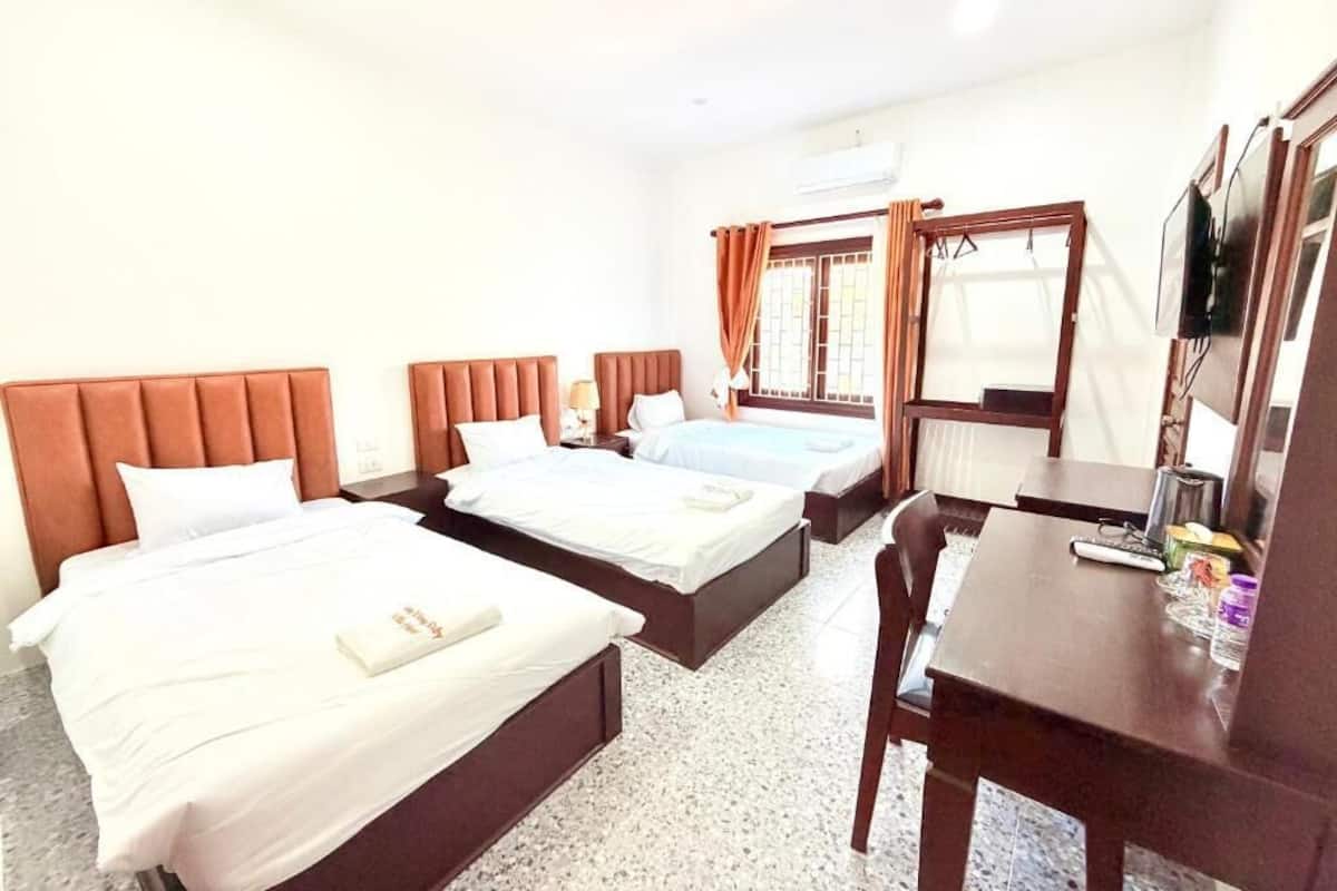 A hotel room with three beds, a desk, and a television.