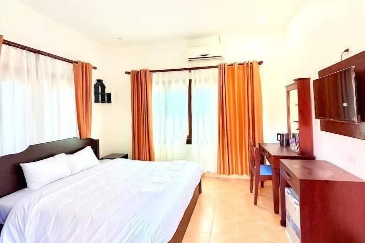 A hotel room with a bed, a desk, a chair, and an air conditioning unit.