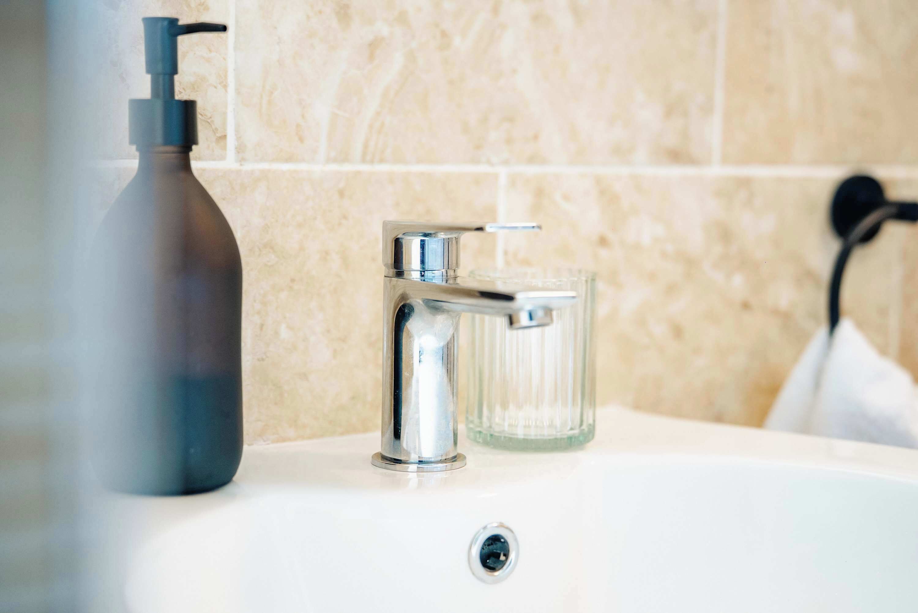 Une salle de bain dotée d’un robinet moderne, d’un distributeur de savon et d’un récipient en verre.