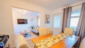 A modern living room with a dining area, a flat-screen TV, a sofa, and a painting on the wall.