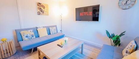 A living room with a sofa, coffee table, and a wall-mounted TV displaying 'NETFLIX'.