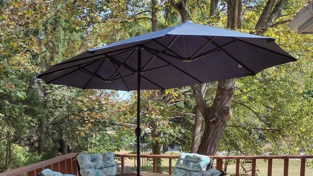 Una terraza de madera con una mesa y sillas bajo un paraguas grande.