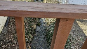 Barandilla de madera con vistas a un arroyo con rocas y follaje.