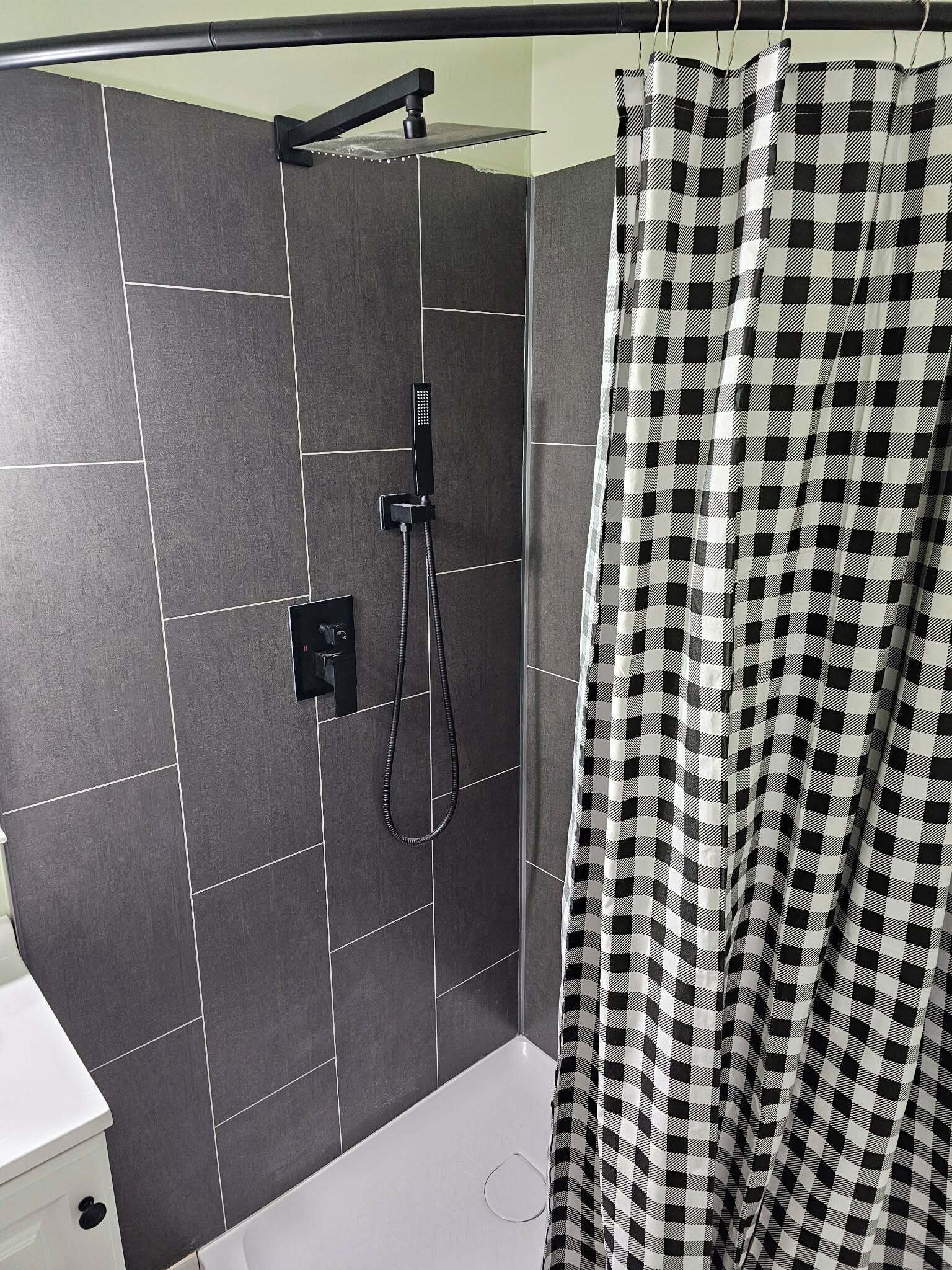 A bathroom with a shower, tiled walls, and a checkered shower curtain.