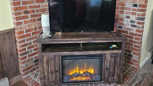 Una chimenea de ladrillo con un televisor encima, un estante pequeño y fuego ardiendo en su interior.