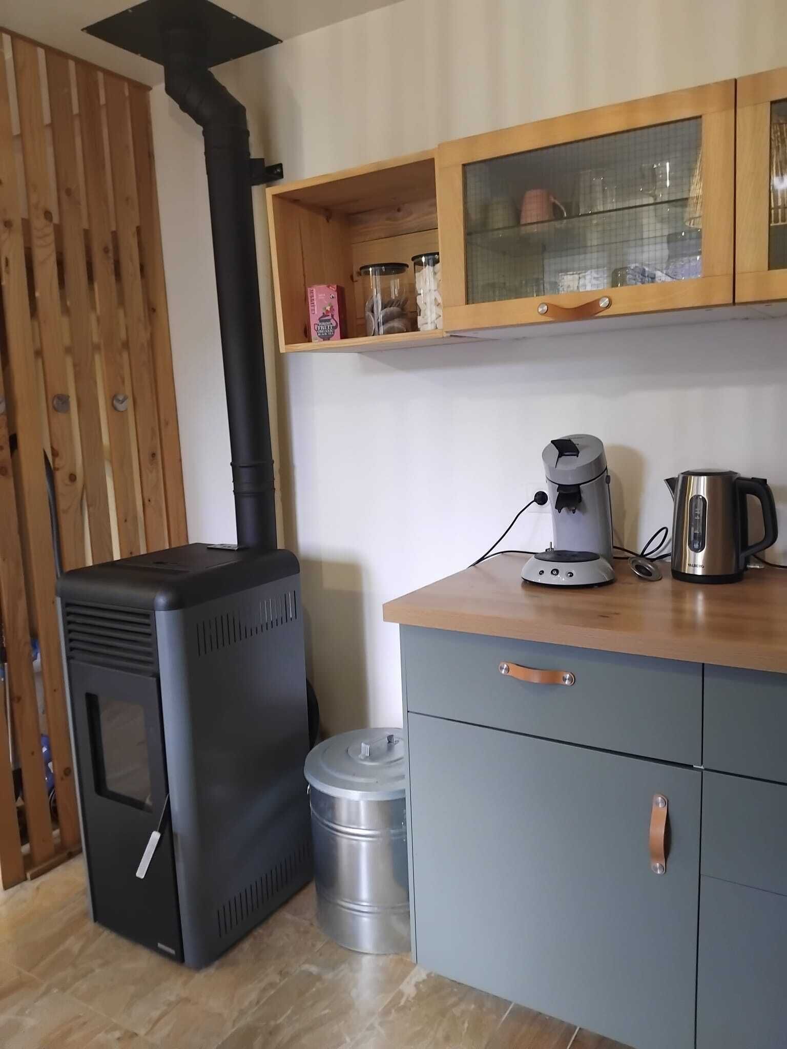 A compact kitchen with a wood-burning stove, a kettle, and a cabinet with glass doors.