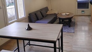 A modern living room with a sofa, a dining table, a small round table, and a hanging light fixture.