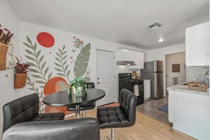A modern kitchen with white cabinets, stainless steel appliances, and a dining area with a round table and leather chairs. - Stunning cozy home with huge backyard (Round Rock)