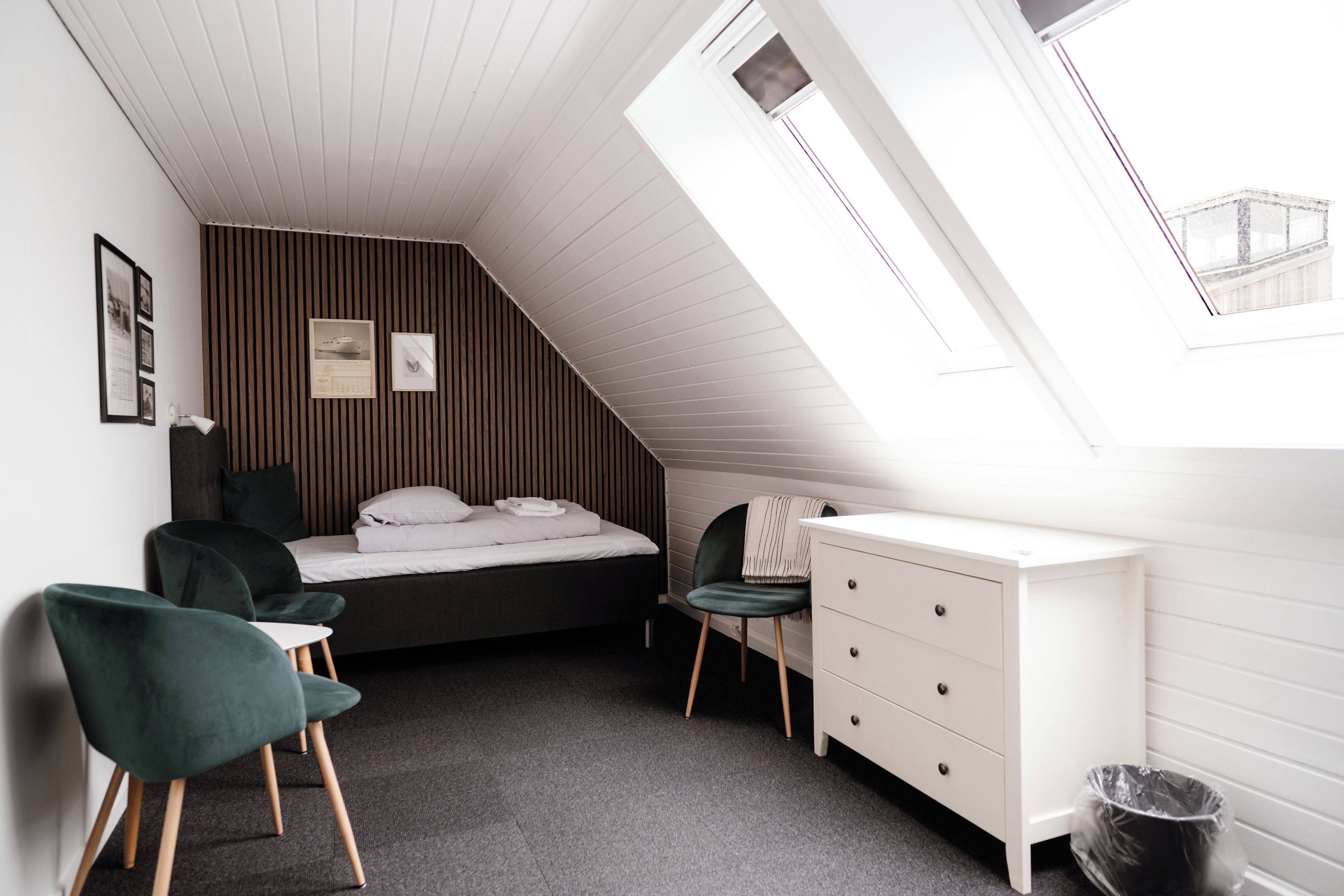 Ein gemütliches Schlafzimmer mit schrägem Dach, einem Bett, einem Schreibtisch, einem Stuhl und einem kleinen Fenster.