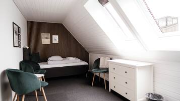 Ein gemütliches Schlafzimmer mit schrägem Dach, einem Bett, einem Schreibtisch, einem Stuhl und einem kleinen Fenster.