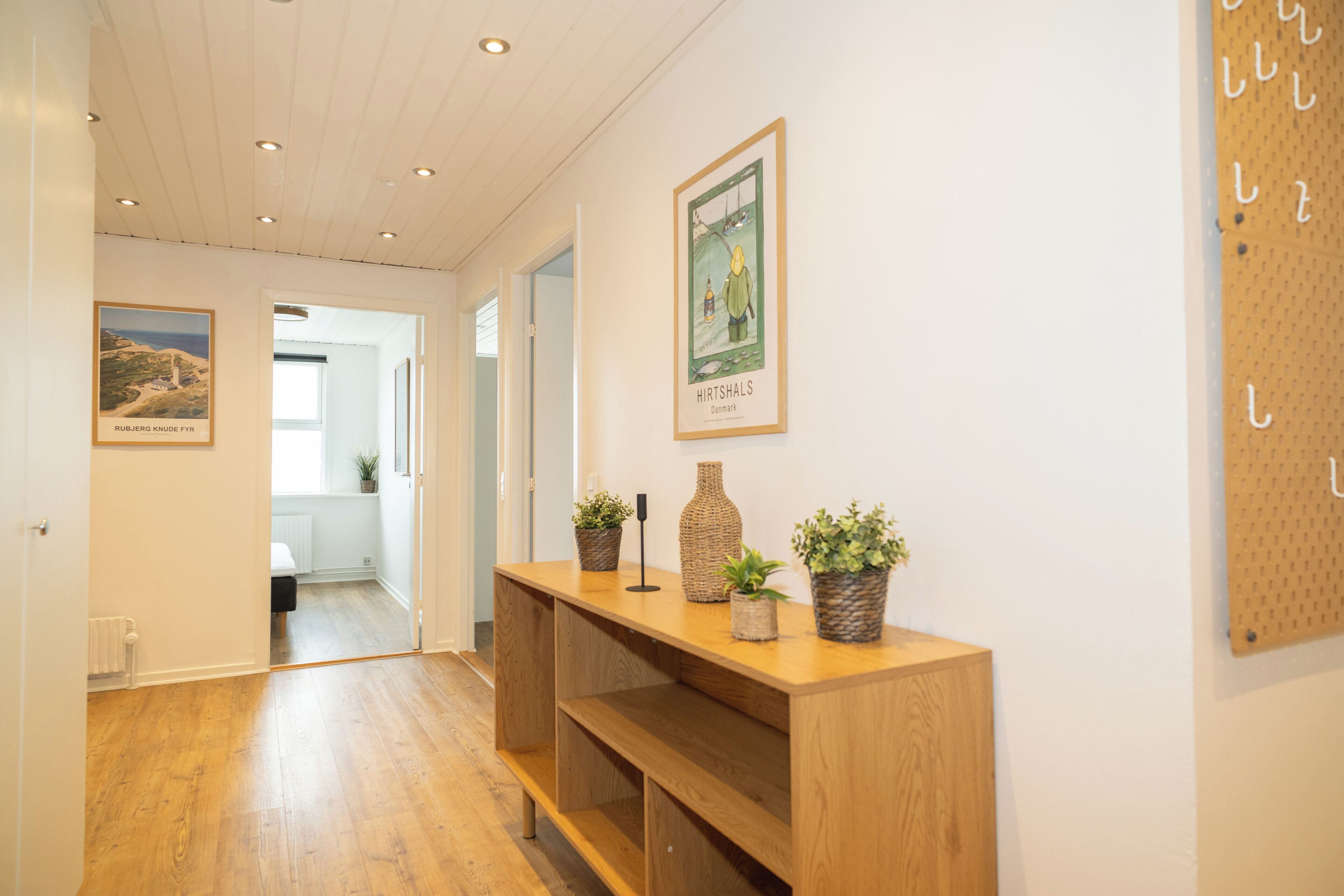 A hallway with wooden flooring, a wooden console table with potted plants, and framed pictures on the walls.