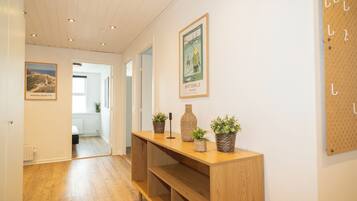 A hallway with wooden flooring, a wooden console table with potted plants, and framed pictures on the walls.
