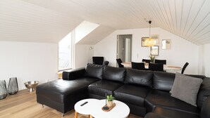 A modern living room with a black leather sectional sofa, a white coffee table, and a dining area with a table and chairs. - B&B by the Sea Hirtshals (Hirtshals)
