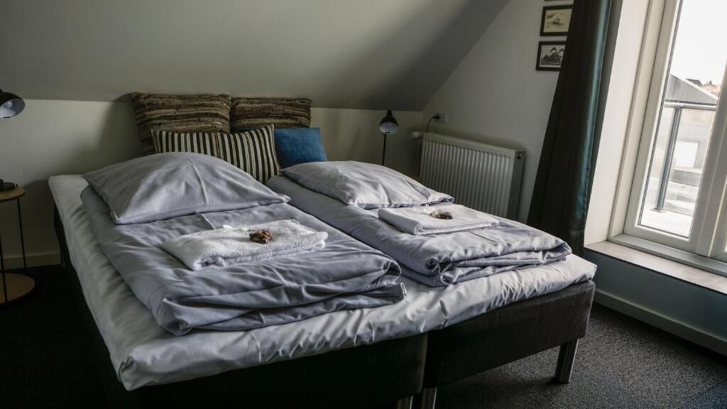 A twin bed with a dark headboard, a bedside table with a lamp, and a window with curtains.