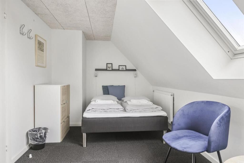 A bedroom with a bed, a chair, a radiator, and a skylight.