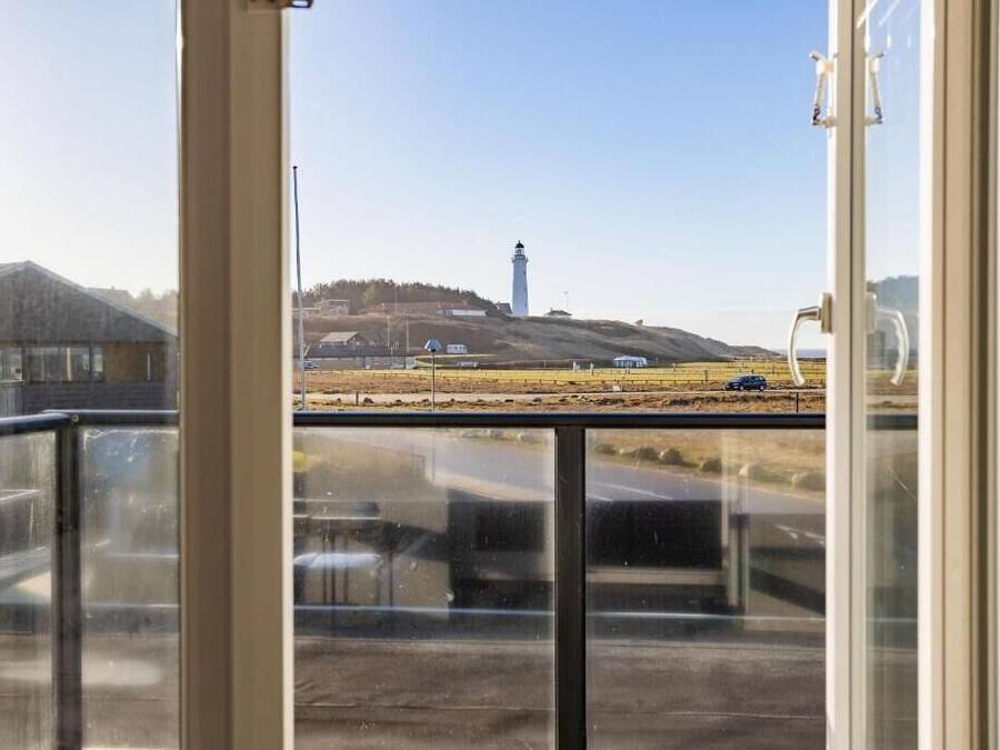A view through a window of a building with a road, a hill, and a lighthouse in the distance.