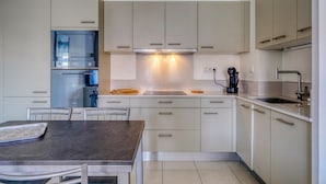 Una cocina moderna con armarios blancos, horno integrado y comedor con mesa y sillas.