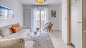 Una sala de estar con un sofá, una mesa de centro, un sillón de mimbre y vistas al exterior a través de un ventanal.