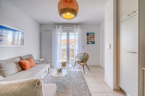 A living room with a sofa, a coffee table, a wicker chair, and a view of the outside through a glass door. - Rivage Apartment, Arcachon (Arcachon)