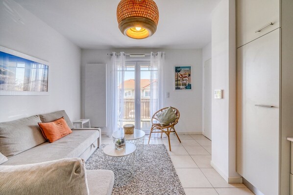A living room with a sofa, a coffee table, a wicker chair, and a view of the outside through a glass door. - Rivage Apartment, Arcachon (Arcachon)