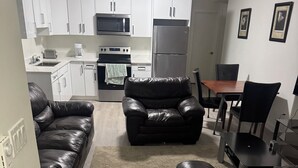 A modern kitchen with white cabinets, a microwave, and a refrigerator. There is a dining area with a table and chairs. - Stylish, conducive, and serene 2-bedroom suite located in the heart of Brighton, (Saskatoon)