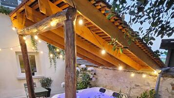 Une pergola en bois décorée de guirlandes lumineuses, un jacuzzi et des plantes en pot, le tout dans un cadre de jardin.