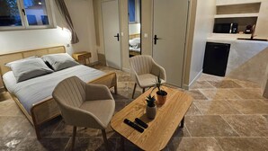 A bedroom with a bed, bedside tables, a chair, a small table with a plant, and a kitchenette area. - THE FRENE SUITE (Montgé-en-Goële)