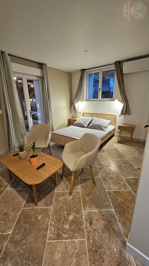 Une chambre d’hôtel avec un lit, deux chaises, une petite table, une fenêtre et une vue sur l’extérieur.