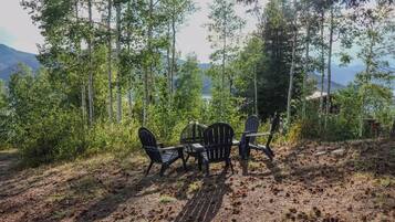 A forested area with a table and chairs, a dirt path, and a cabin in the background.