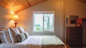 Ein Schlafzimmer mit einem Bett, Kissen, einer Lampe, einem Schminktisch und einem Fenster mit Blick.