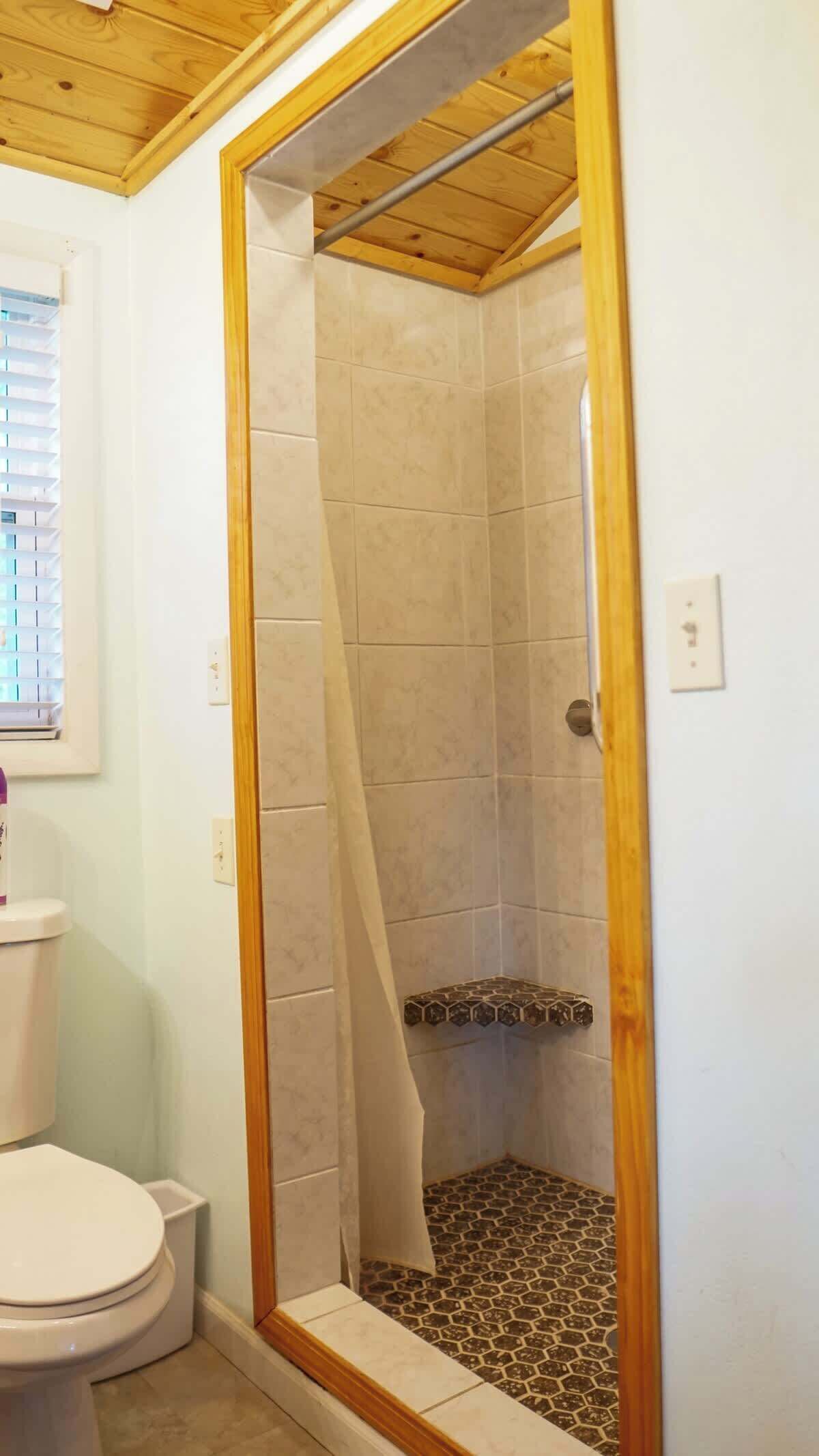 Et badeværelse med brusekabine, toilet og et vindue med rullegardiner.