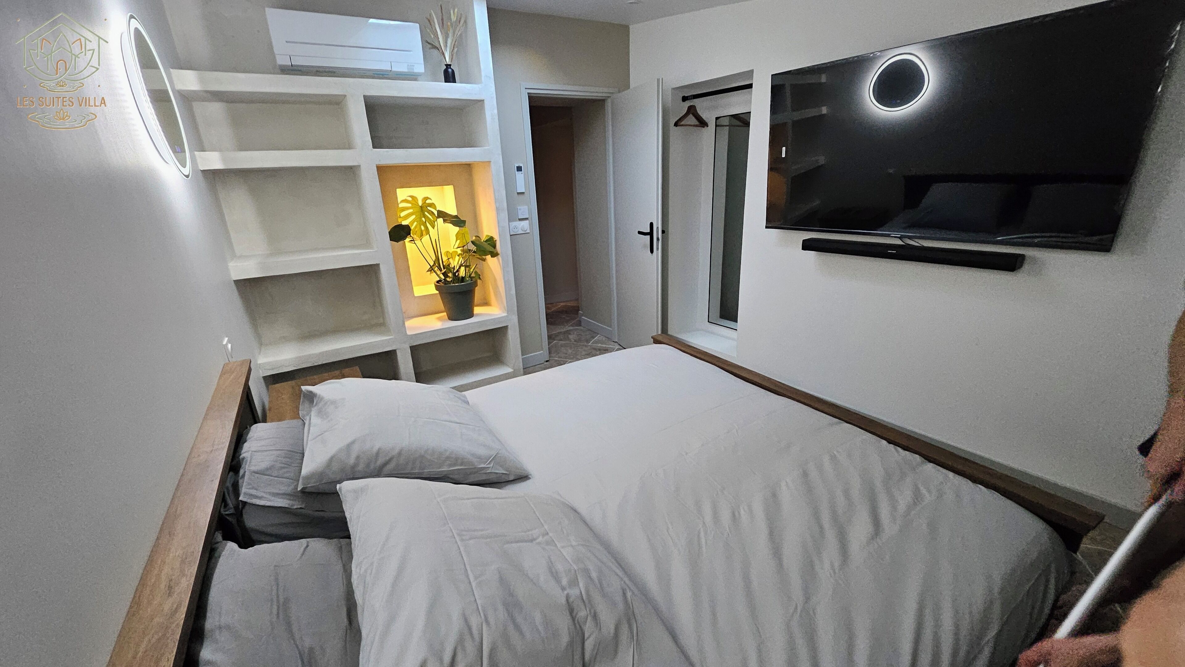 A bedroom with a bed, a TV, a wardrobe, and a potted plant.