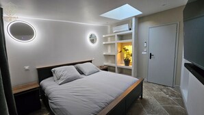 Une chambre moderne avec une lucarne, un lit avec une literie grise, des tables de chevet et des étagères intégrées agrémentées d’une plante.