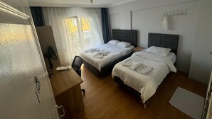 A hotel room with two beds, a desk, a chair, a ceiling fan, and a window with curtains. - Filyos Lotus Pansiyon (Caycuma)