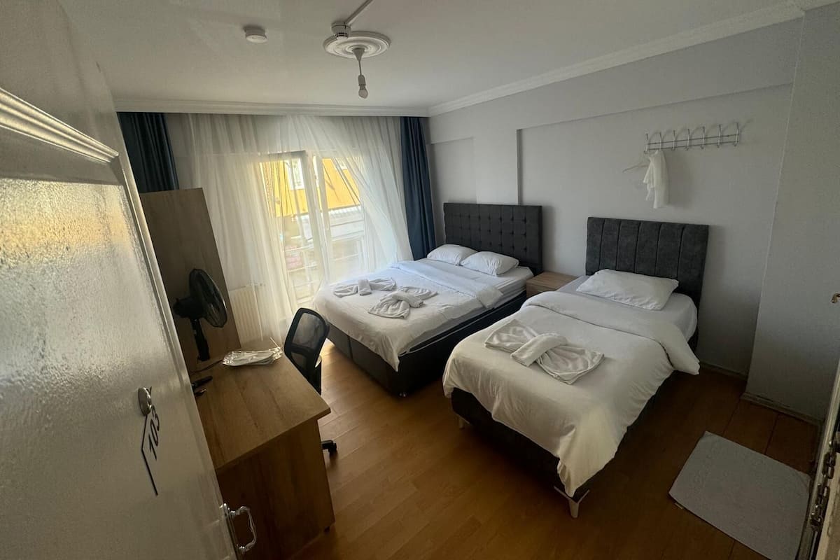 A hotel room with two beds, a desk, a chair, a ceiling fan, and a window with curtains.