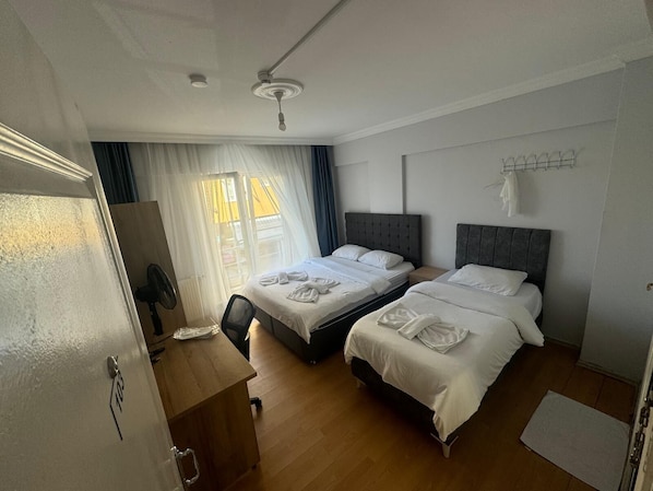 A hotel room with two beds, a desk, a chair, a ceiling fan, and a window with curtains.