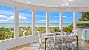 Un comedor con vista al océano, amplias ventanas y una lámpara de techo moderna.