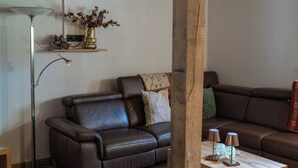 A living room with a brown leather sofa, a wooden coffee table, a floor lamp, and a vase with dried flowers on a shelf. - Exceptional "Kiefer" vacation apartment (Dötlingen)