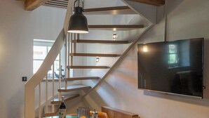 A dining area with a round table, chairs, a television mounted on the wall, and a wooden staircase. - Exceptional "Kiefer" vacation apartment (Dötlingen)