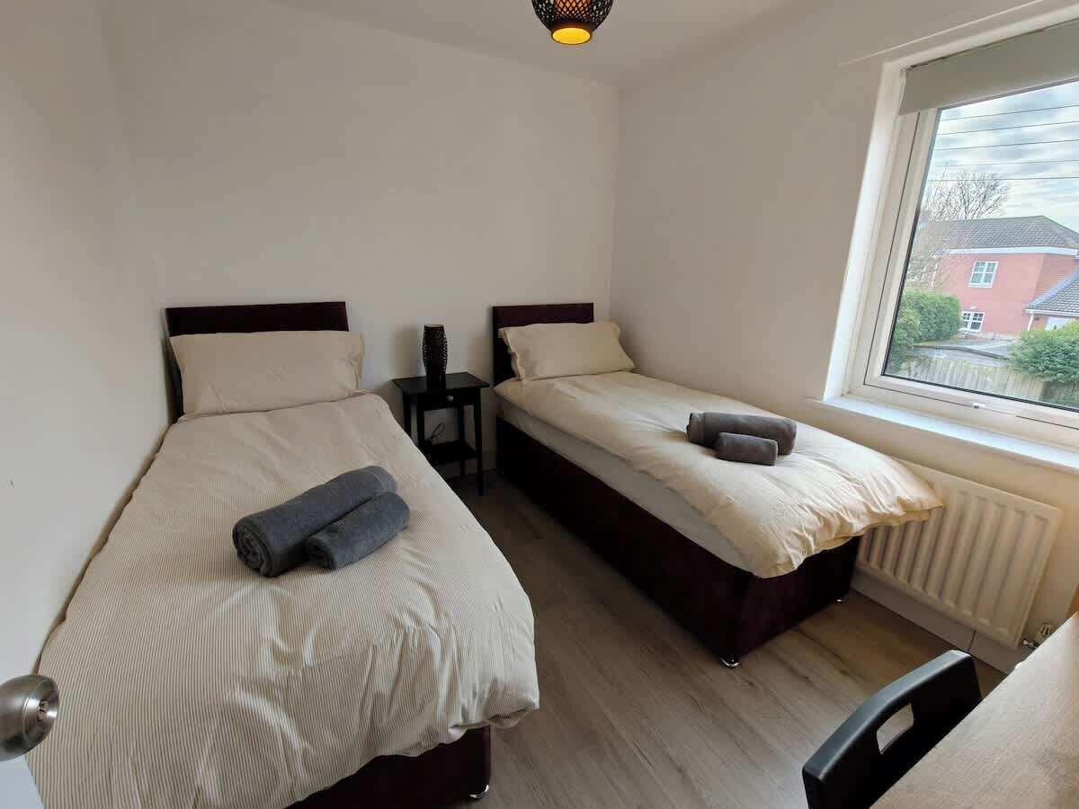 A room with two beds, a radiator, a window with a view, and a door.