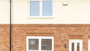 Ein zweistöckiges Haus mit Ziegelaußenwand, einer weißen Tür und einem Fenster mit Gitterstäben.