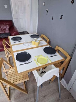 Una mesa de comedor con cuatro sillas, un mantel blanco y un juego de platos, tazas y cubiertos.