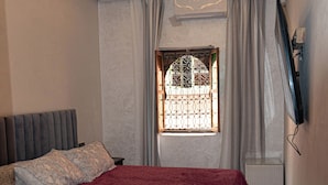A bedroom with a bed, a window with curtains, a ceiling light fixture, and a wall-mounted television. - Dar Medina (Marrakech)