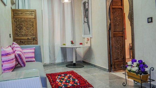 A room with a sofa, a patterned rug, a small table with a vase, and a wooden door. - Dar Medina (Marrakech)