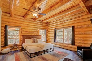 Ein Schlafzimmer in einer Blockhütte mit einem Bett, einem Deckenventilator und großen Fenstern.